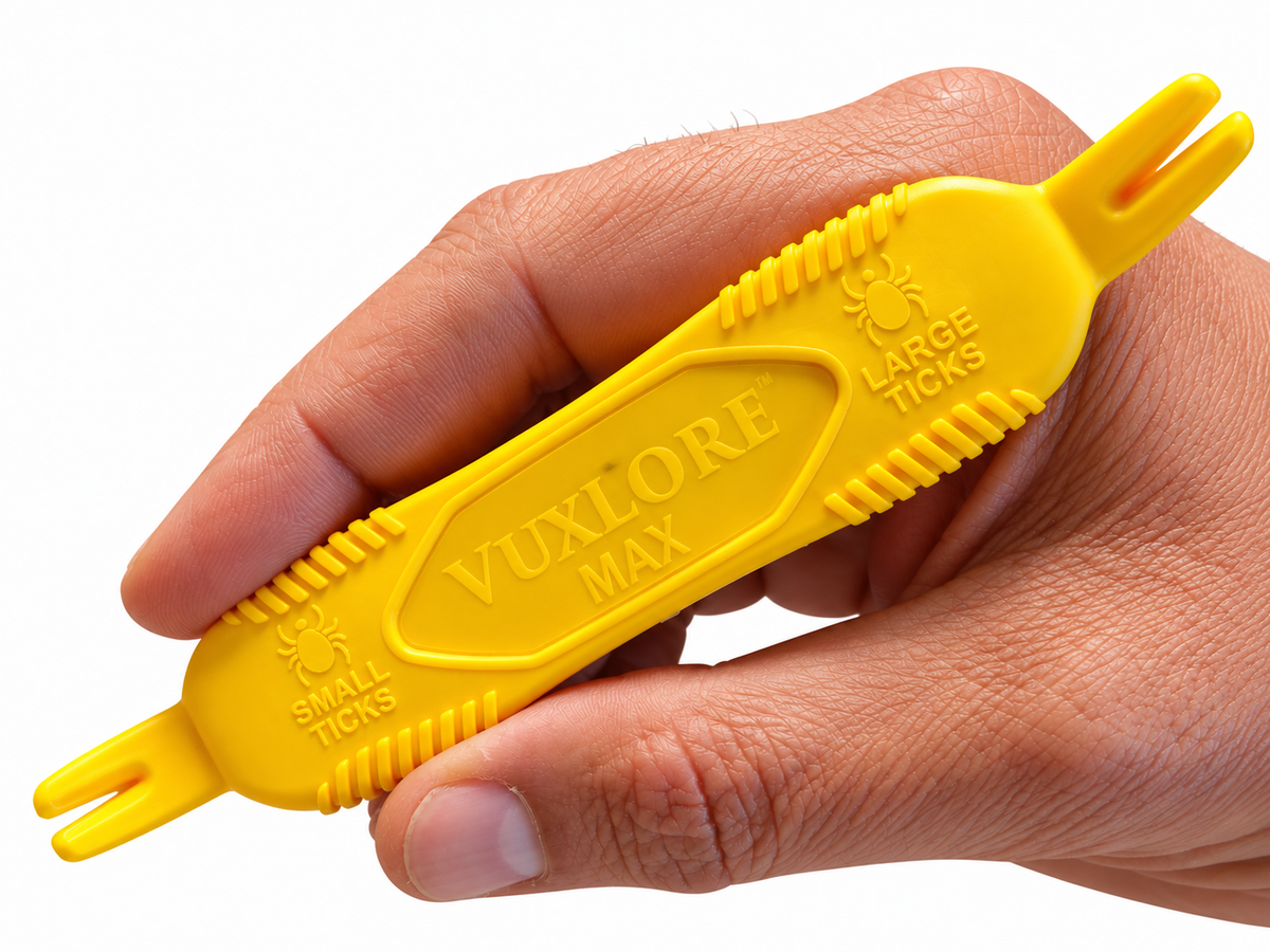 Close-up of a hand holding the yellow VuxLore MAX tick remover, showing textured grip ridges and forked ends labelled for small and large ticks.